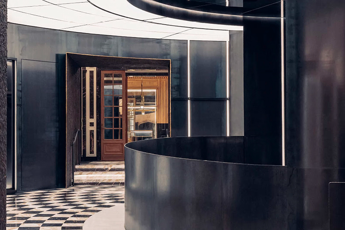 Moncler boutique interior with dark steel curved walls, a chequered floor and a wooden door in the background.