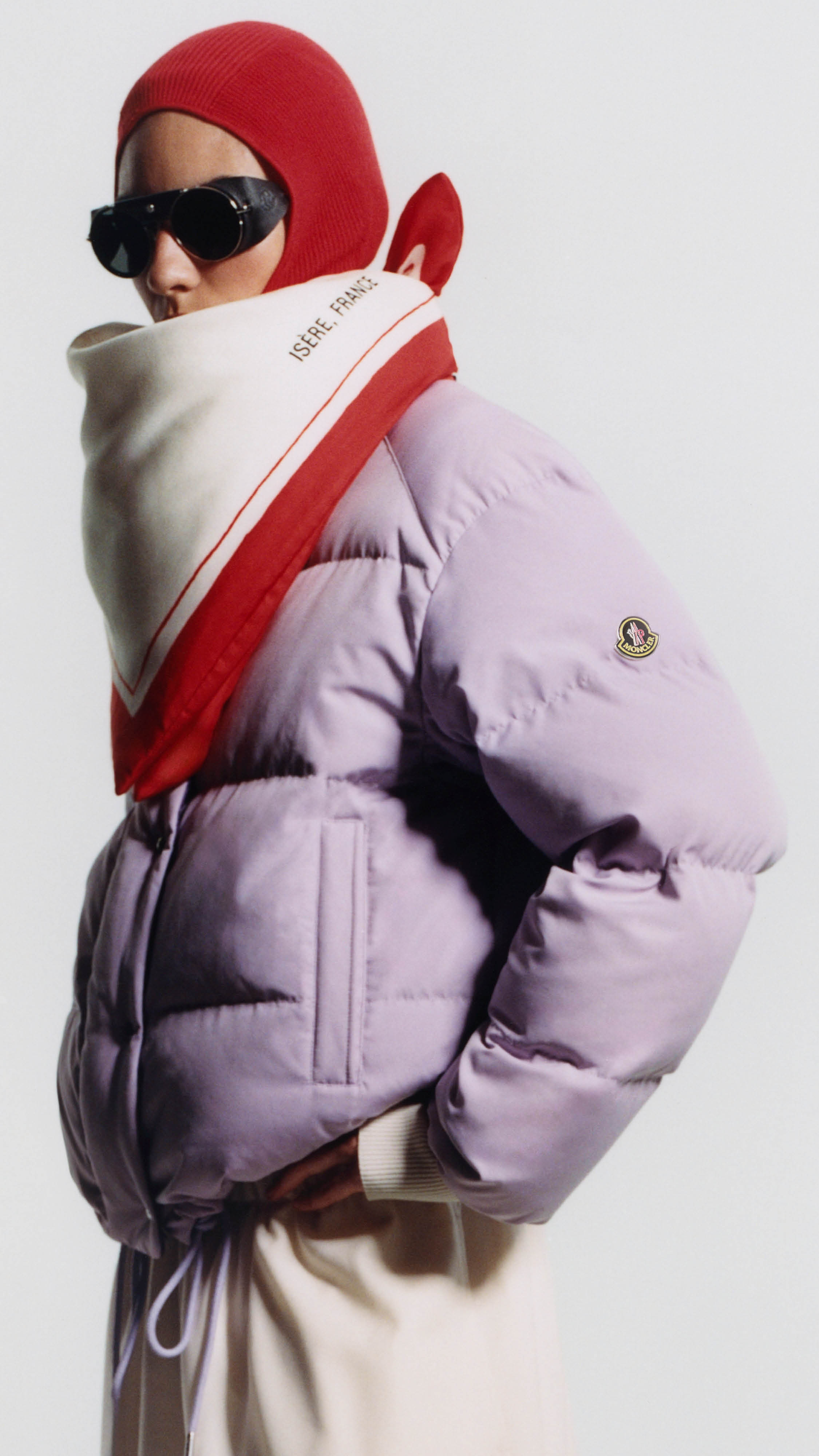 Moncler Re/Icons 2026, lilac Verone down jacket, red balaclava, printed scarf and black sunglasses. 