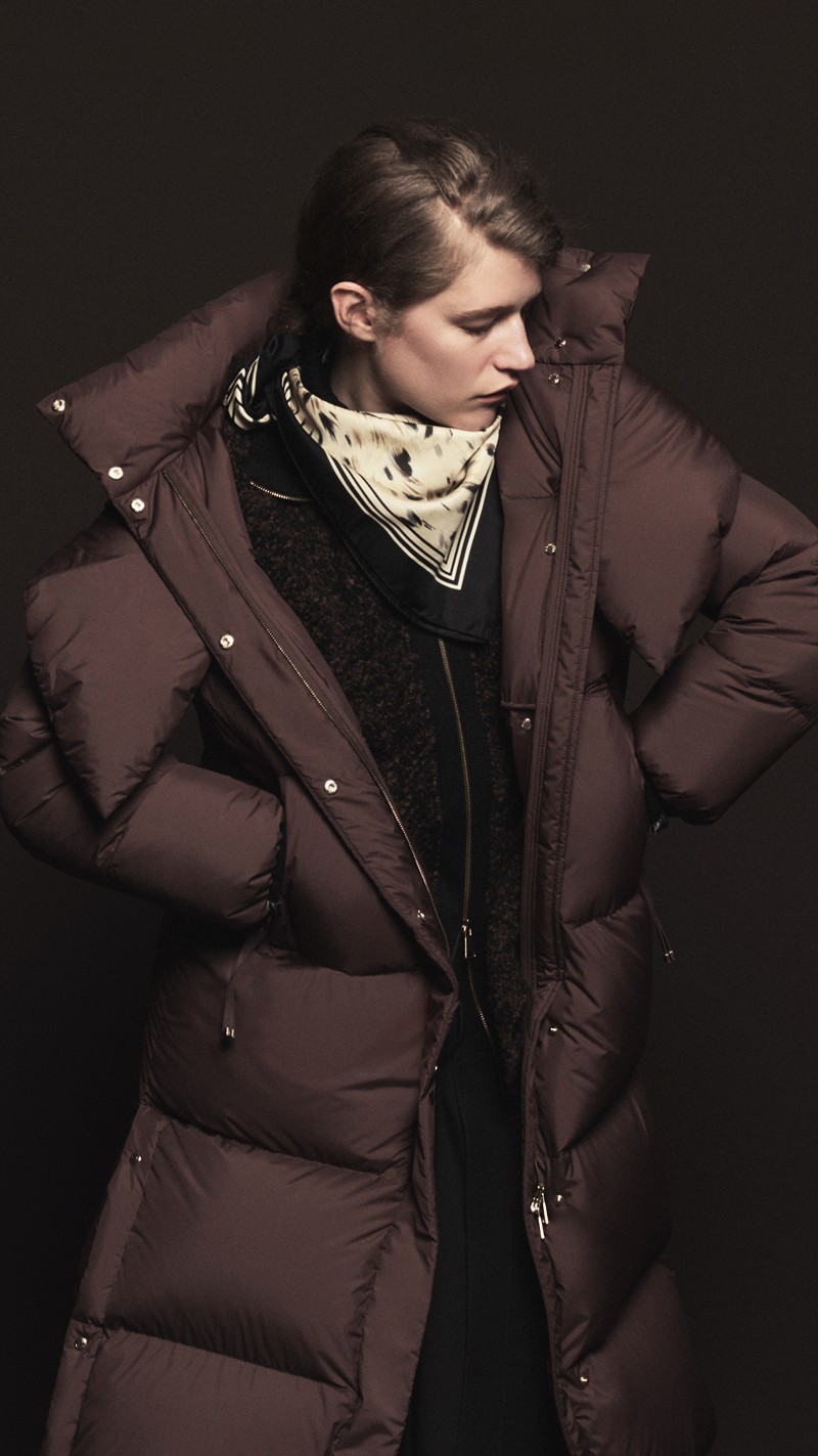 Moncler Fall/Winter 2026 for men and women. Oversized burgundy down jacket with hood, printed cream scarf and black zip knit.