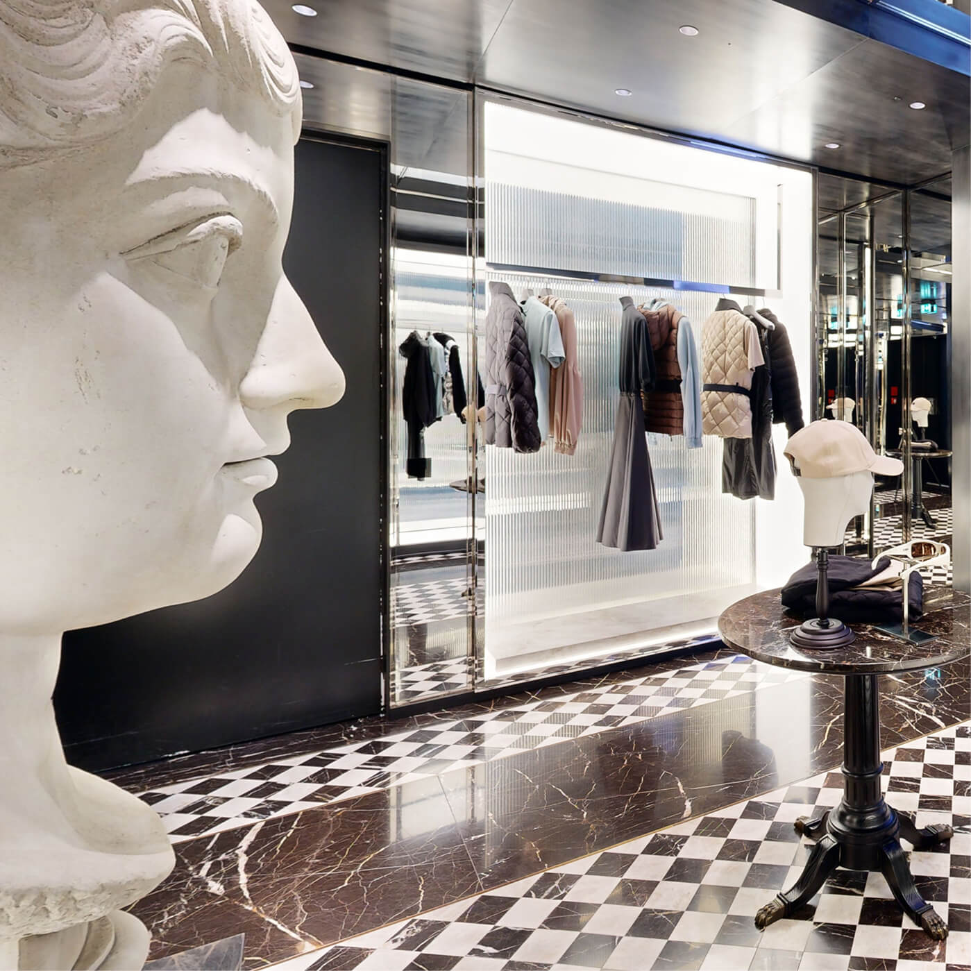 New Moncler Bond Street boutique interior with a marble bust, a Moncler outerwear rail and a table with accessories.