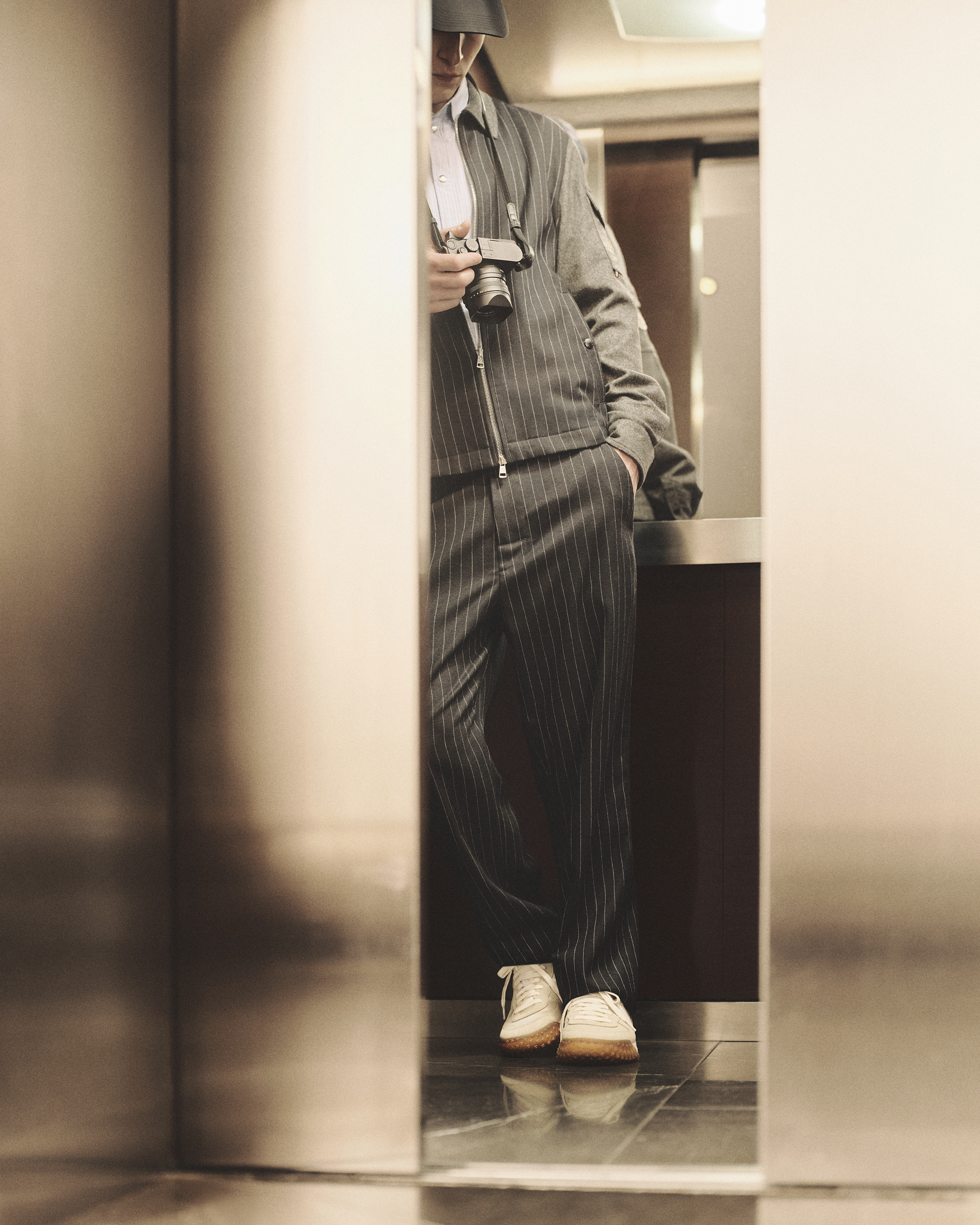 Moncler CityTrek: white and beige sneakers with rubber sole and pinstripe trousers.