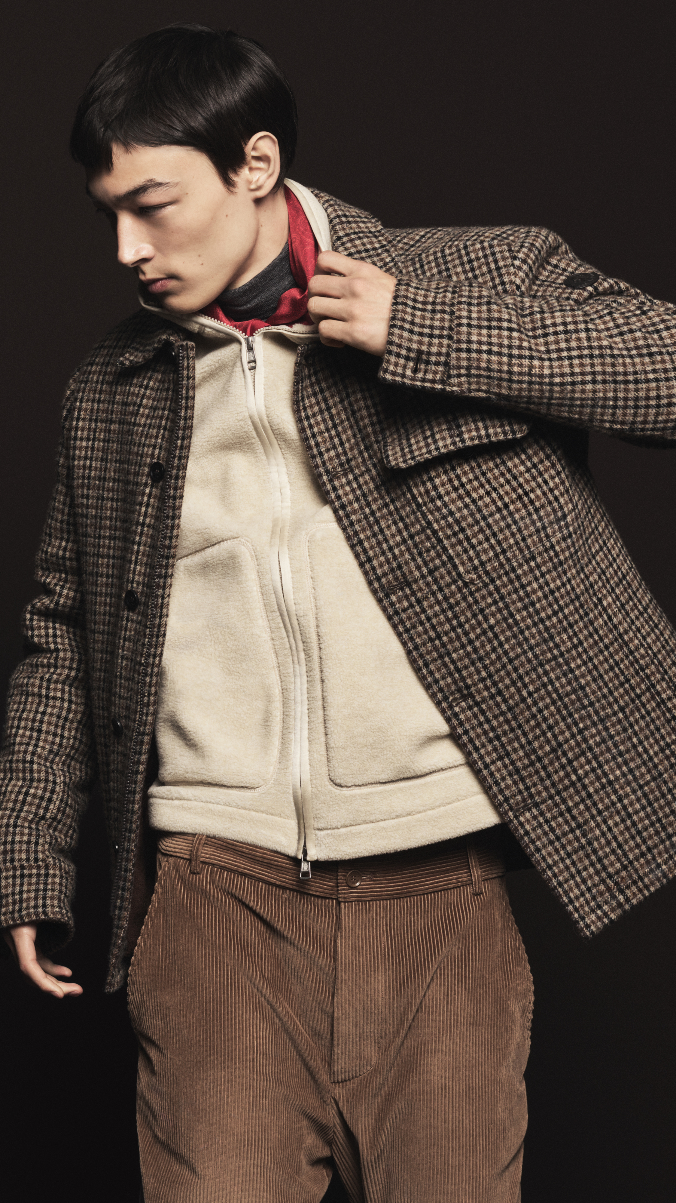 Moncler Fall/Winter 2026 for men and women. Brown checked jacket, cream sweatshirt, red scarf, grey t-shirt, brown trousers.