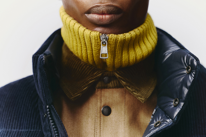 Close-up of a model wearing a yellow knit turtleneck layered with a Moncler down jacket.