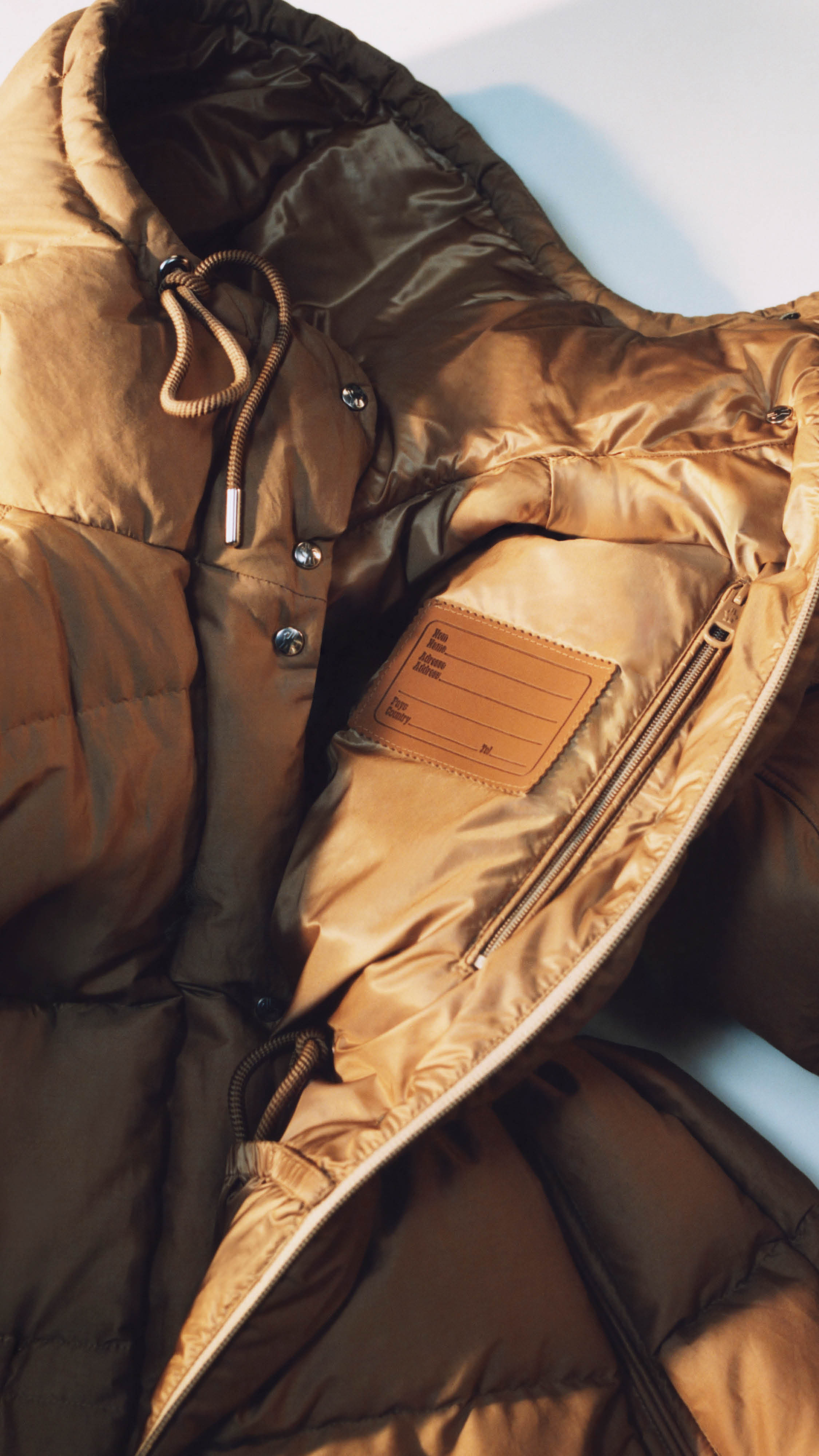 Moncler Re/Icons 2026, inside of a camel Himalaya down jacket with a leather name label.