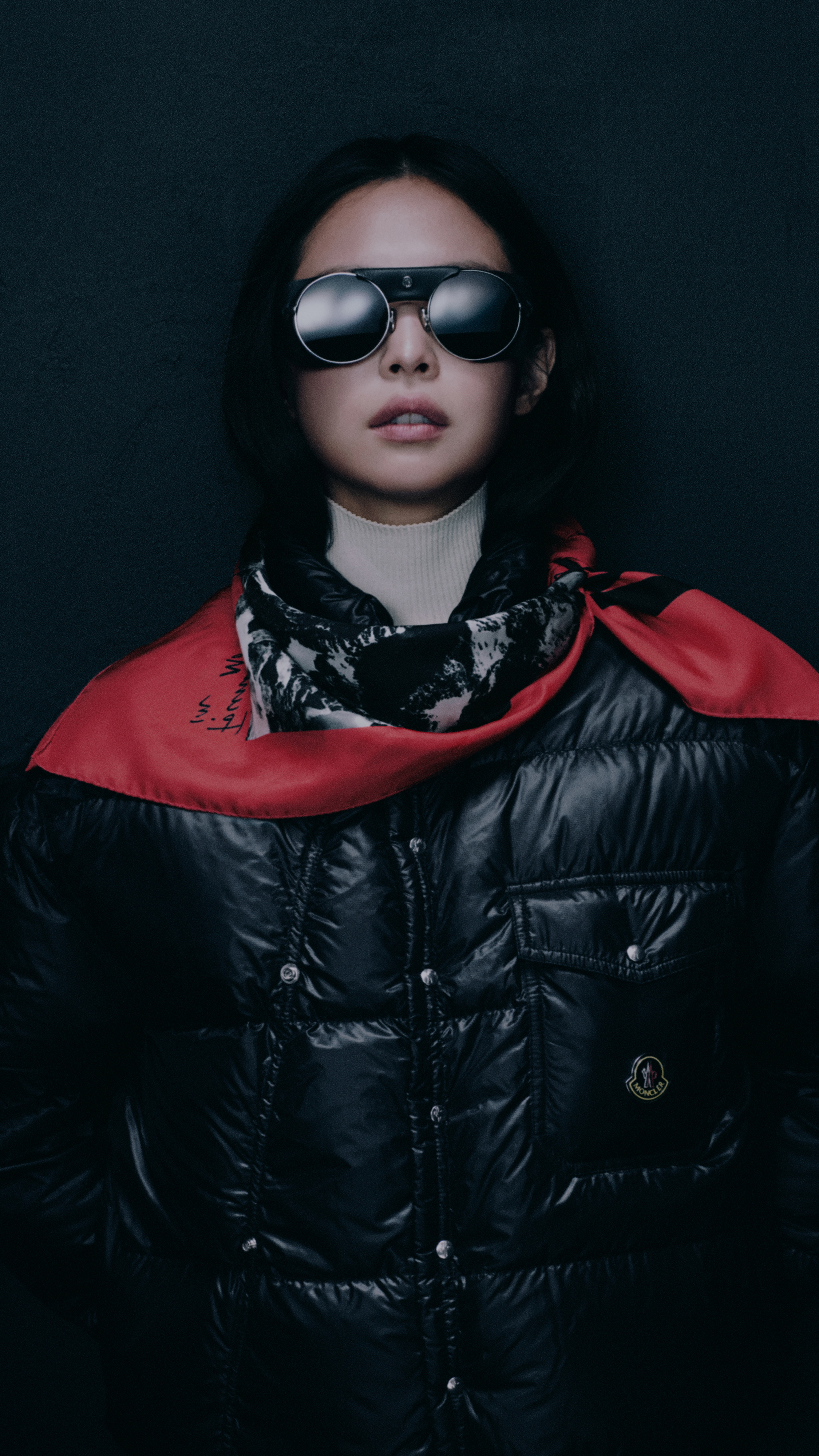 Moncler Re/Icons 2026, Pioneers in Moncler: Jennie in sunglasses, a glossy black down jacket and a red printed scarf.