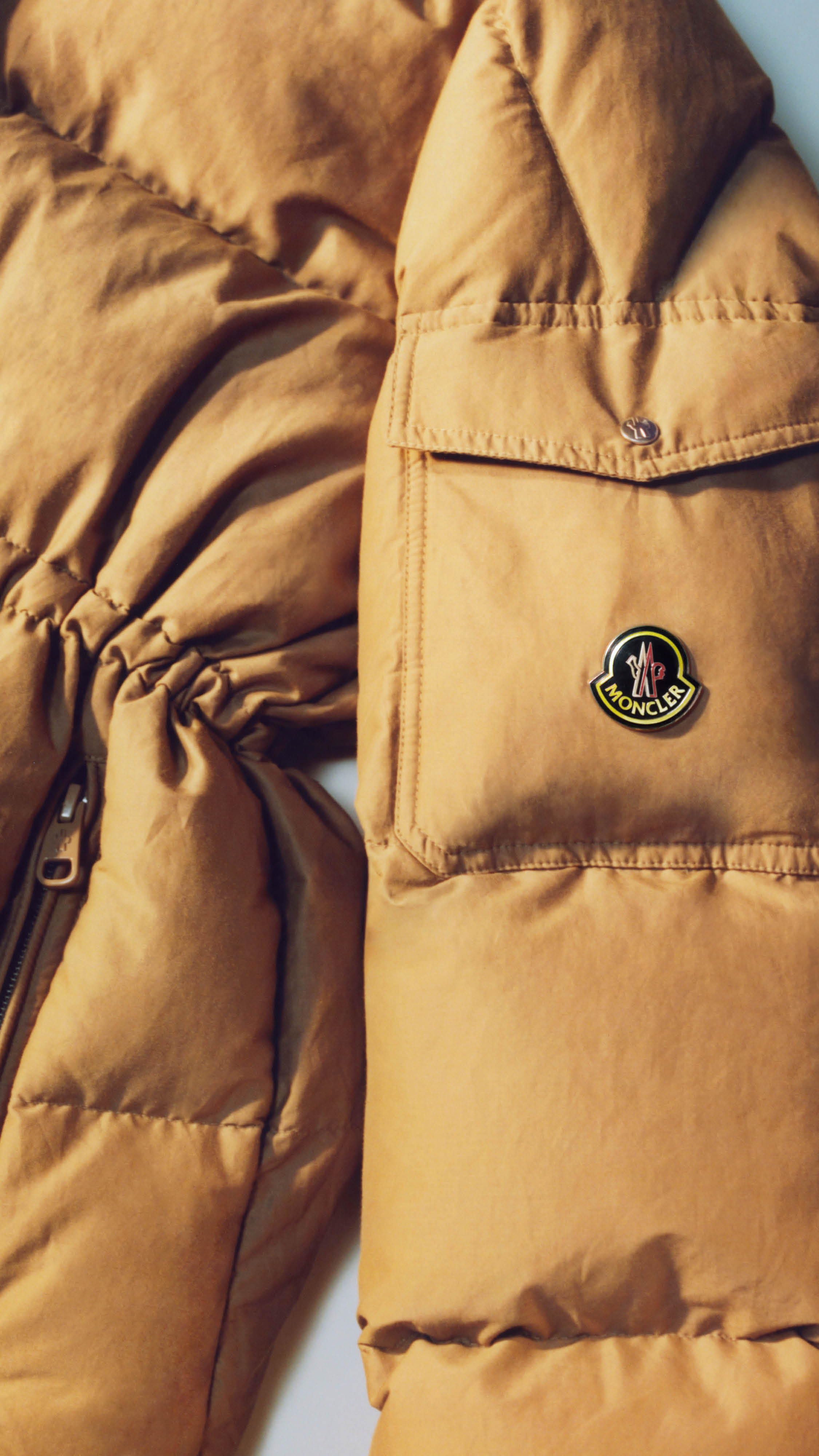 Moncler Re/Icons 2026, pocket of a camel Himalaya down jacket with metal Moncler logo badge.