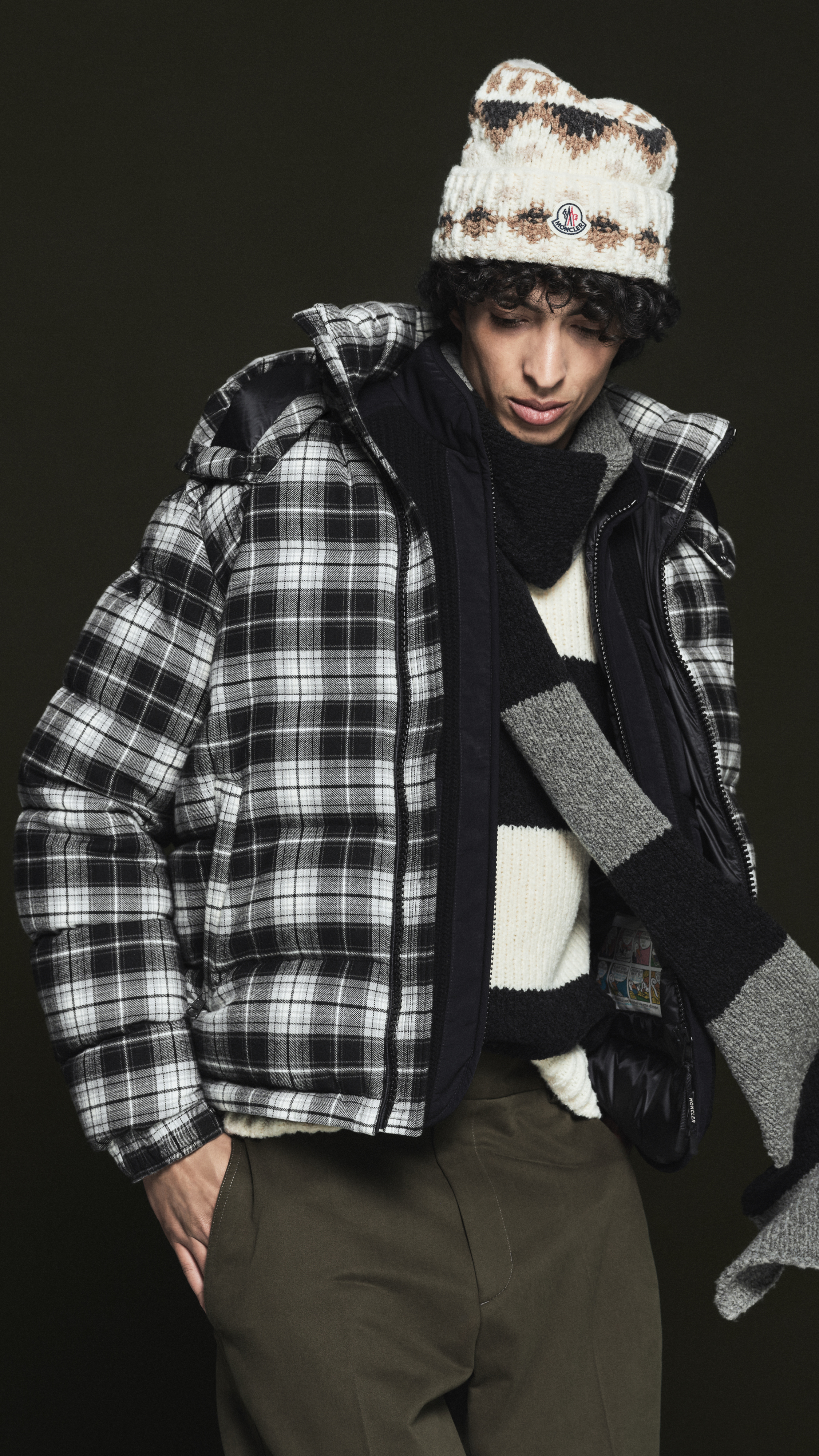 Moncler Pre Fall 2026 for men and women. Wool beanie, checked down jacket, striped scarf and sweater, olive trousers.