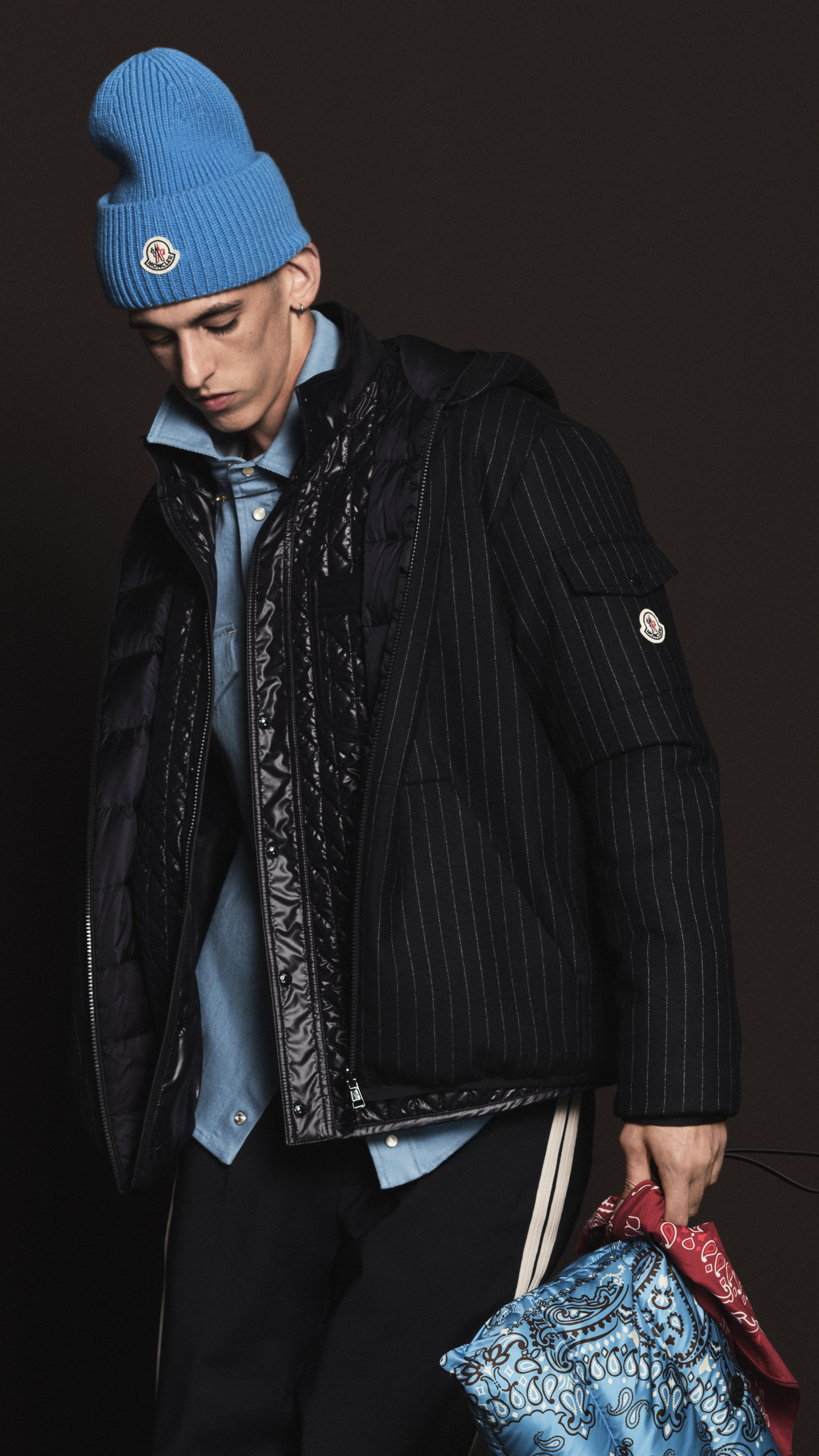 Moncler Pre-Fall 2026 : mannequin en doudoune noire brillante sur veste à fines rayures et chemise en denim
