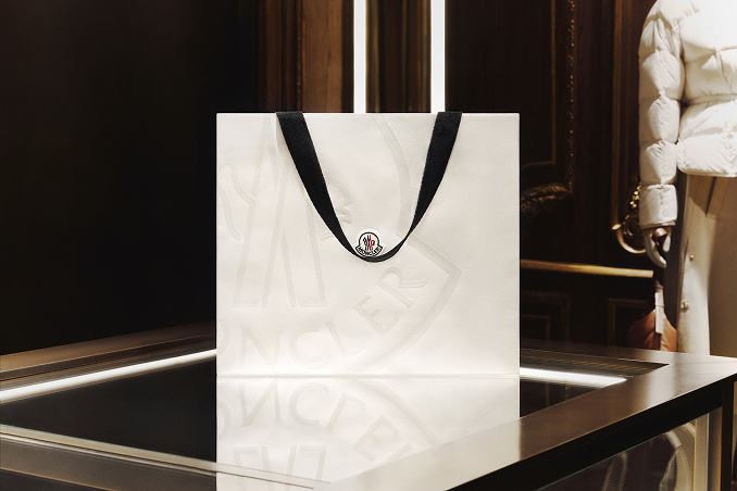 Moncler white shopping bag with black ribbon handles on a dark boutique counter.