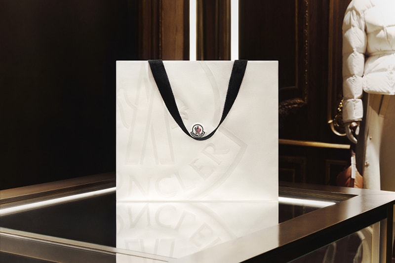 Moncler white shopping bag with black ribbon handles on a dark boutique counter.
