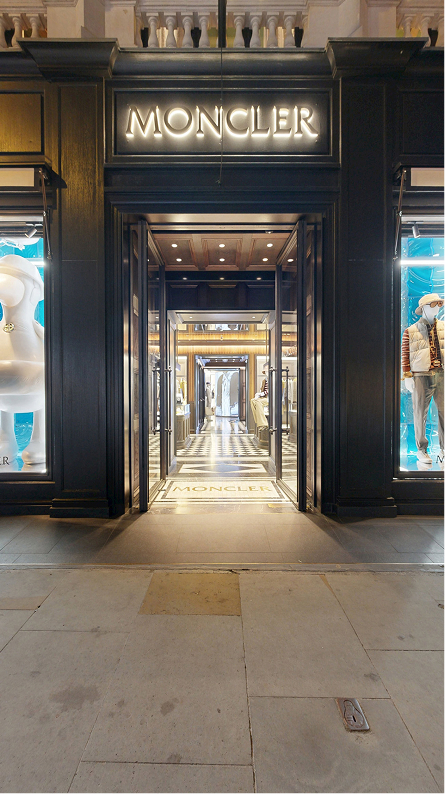 New Moncler Bond Street boutique exterior at night, with two lit display windows with campaign imagery and mannequins.