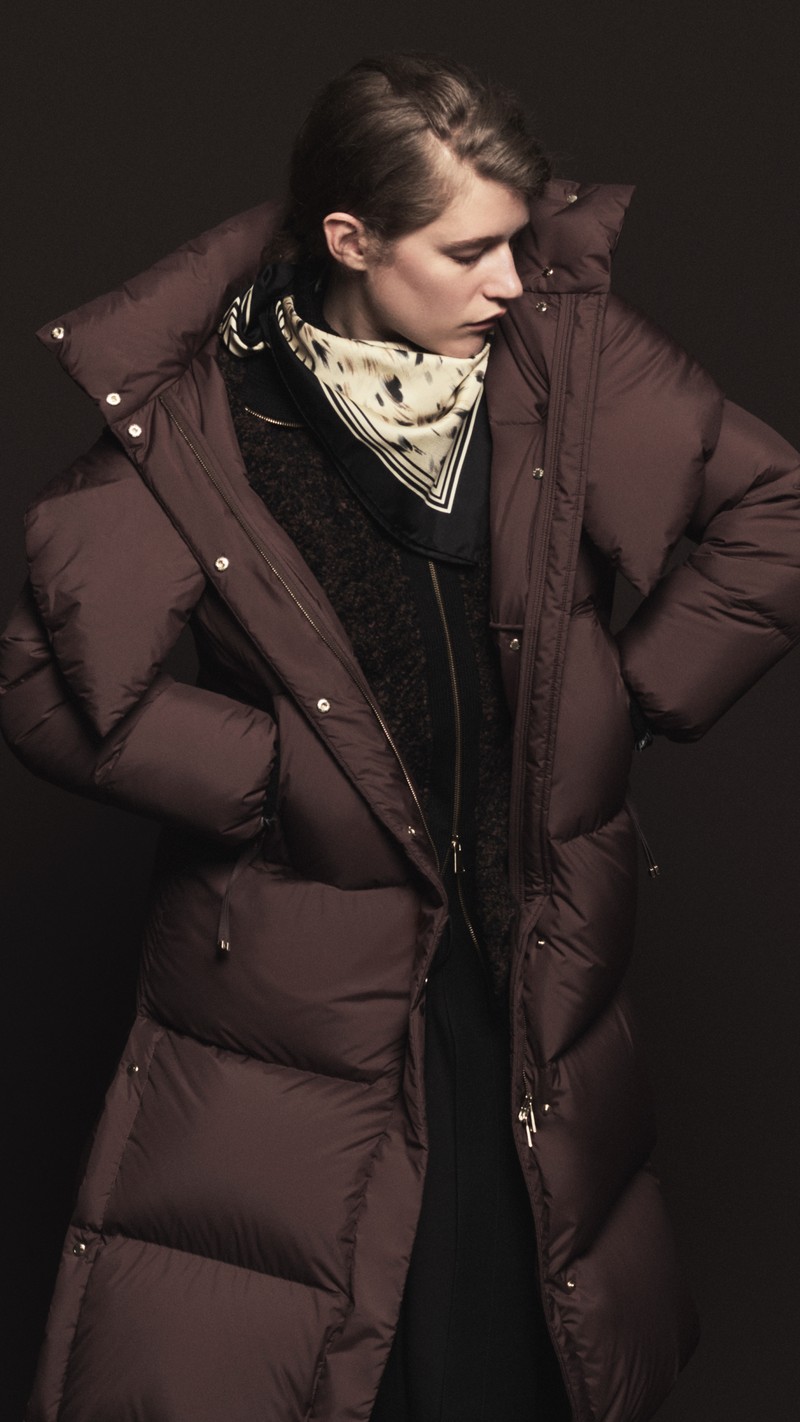 Moncler Fall/Winter 2026 for men and women. Oversized burgundy down jacket with hood, printed cream scarf and black zip knit.