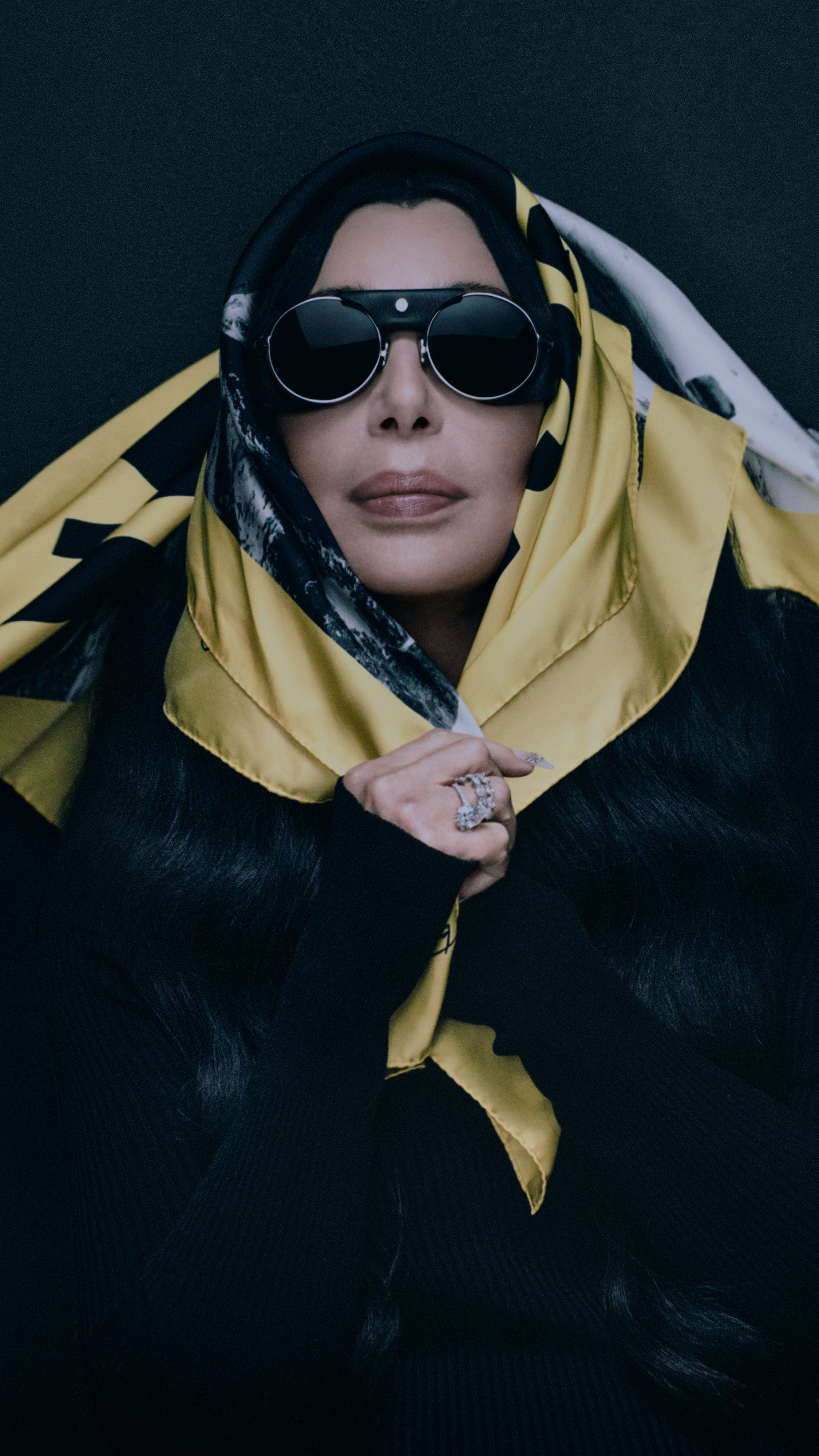 Moncler Re/Icons 2026, Pioneers in Moncler: Cher in round sunglasses wrapped in a yellow and black printed silk scarf.