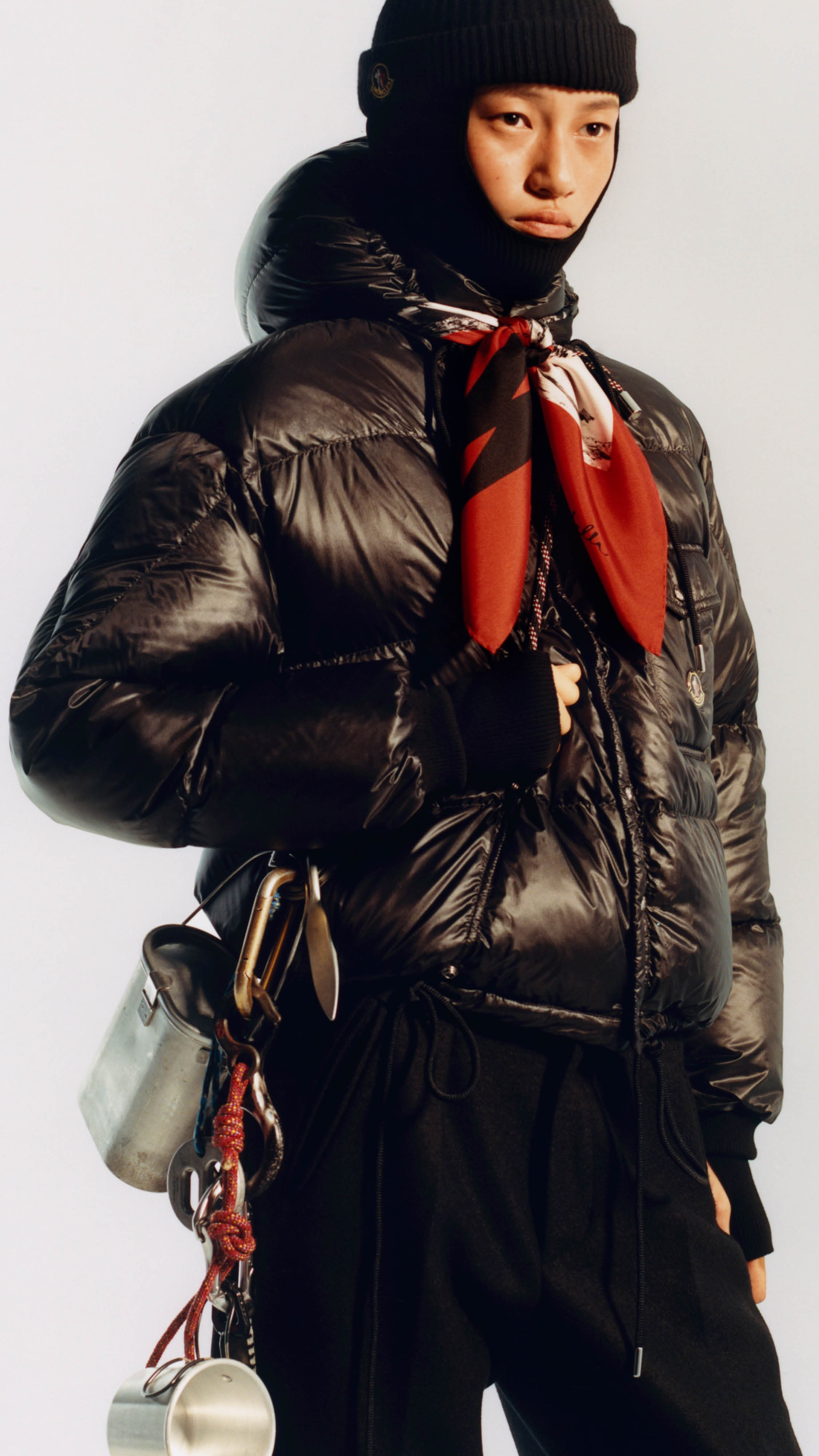 Moncler Re/Icons 2026, black Karakorum down jacket and balaclava, with a red scarf and climbing gear at the hip. 